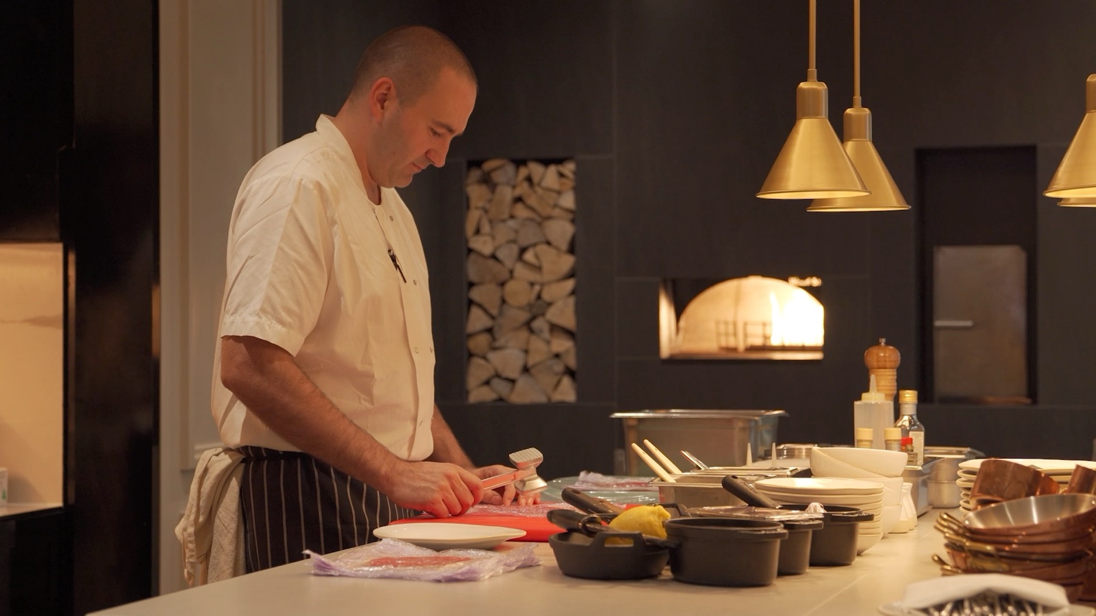 Frame from the Kitchen at Holmes cinemagraph, a chef preparing fish at the pass under brass lights